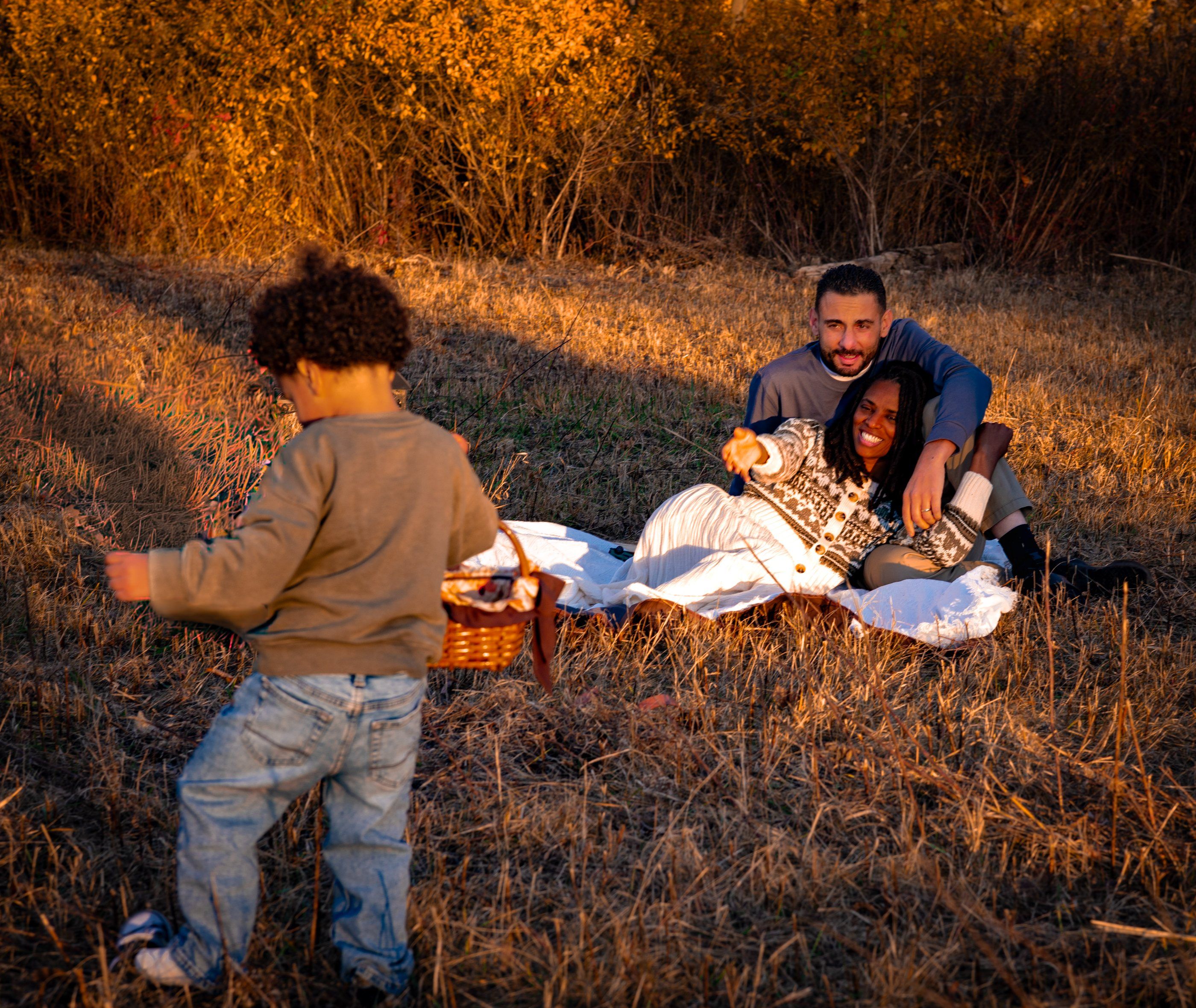 A toddler walking toward his parents on a picnic blanket in autumn light