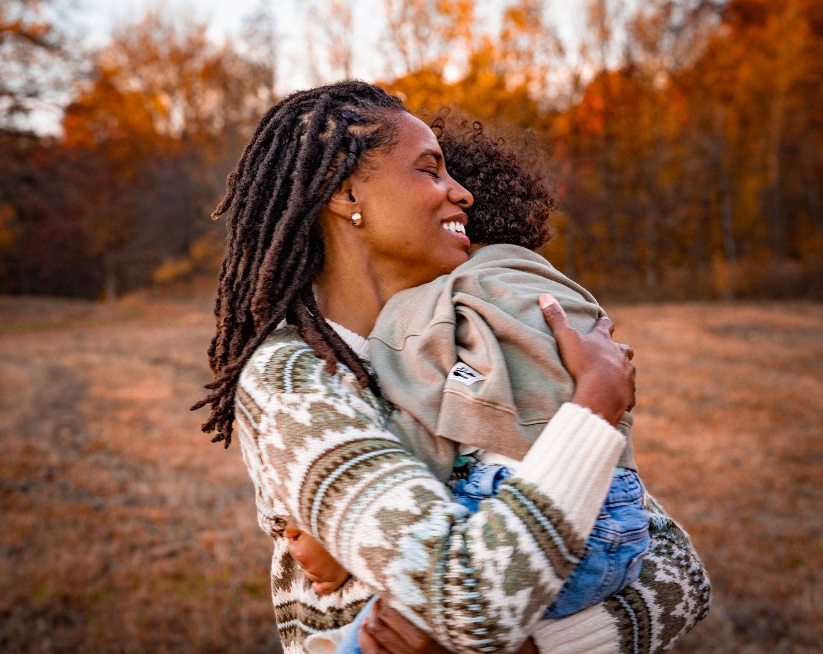 A mother hugging her child close in autumn light