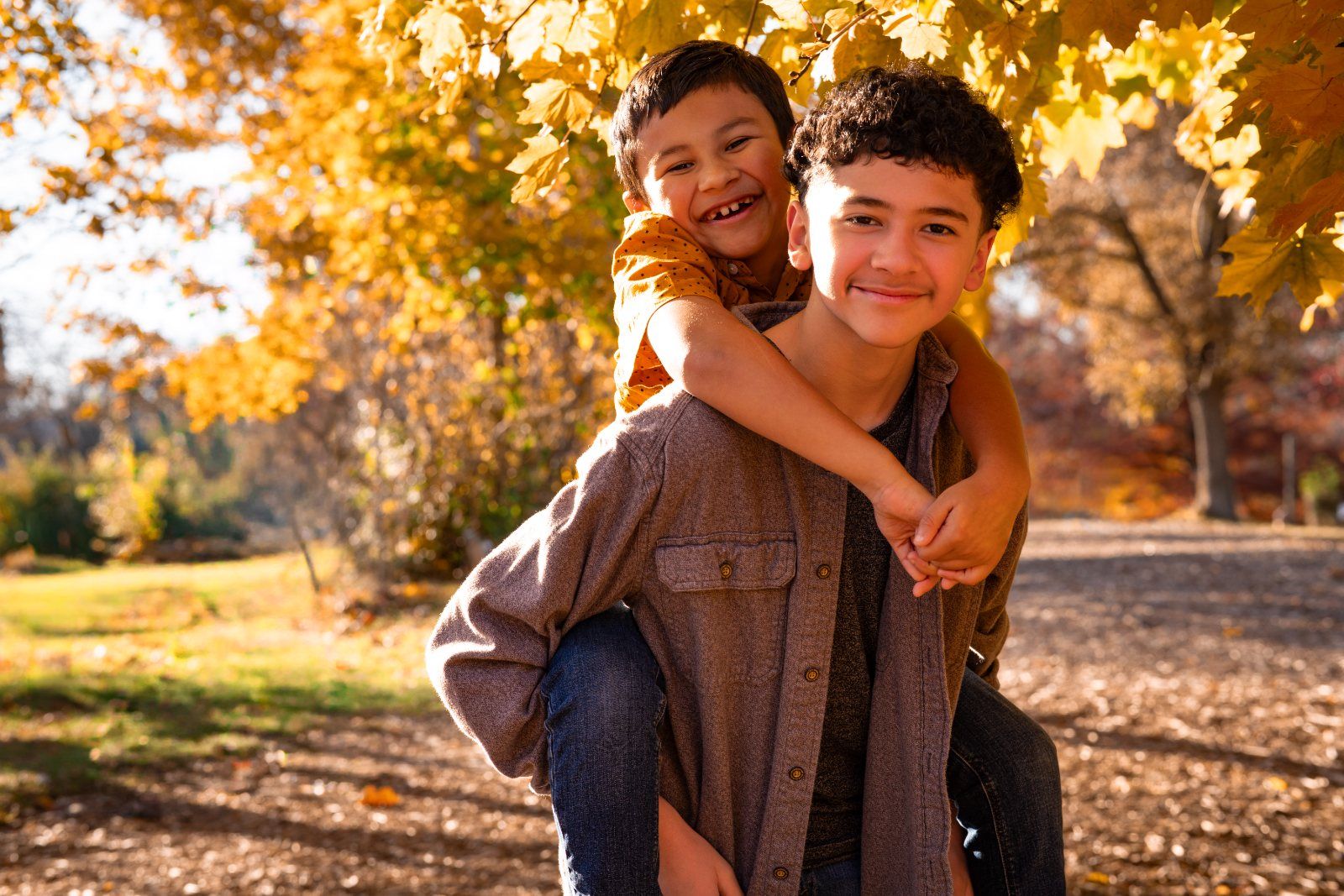 A big brother giving his little brother a piggyback ride under autumn trees