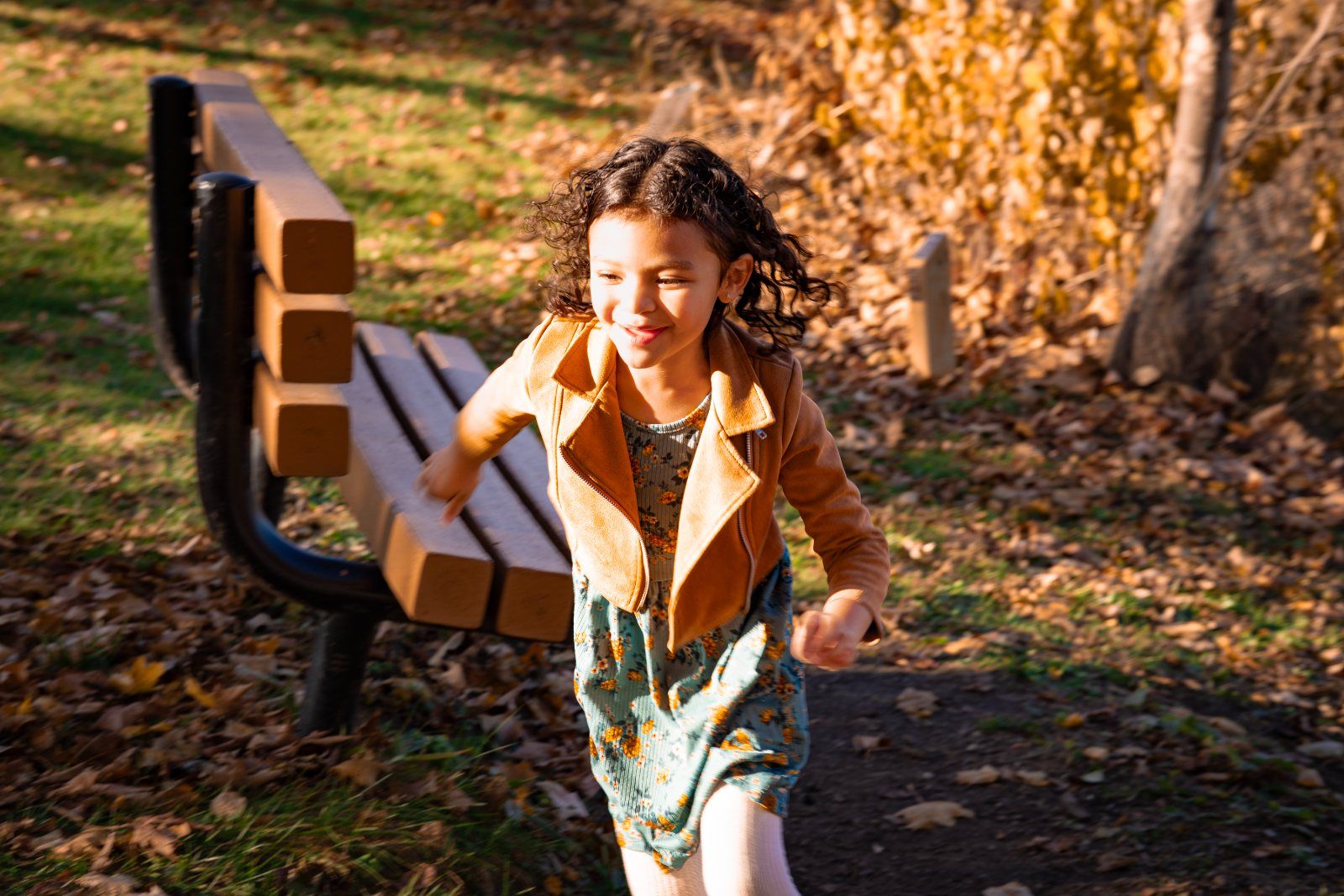 A girl running past a park bench through fallen leaves