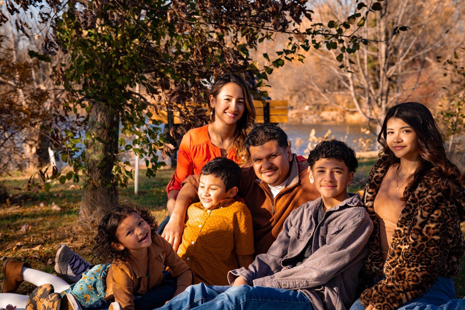 A family of six gathered on a blanket by the lake in autumn