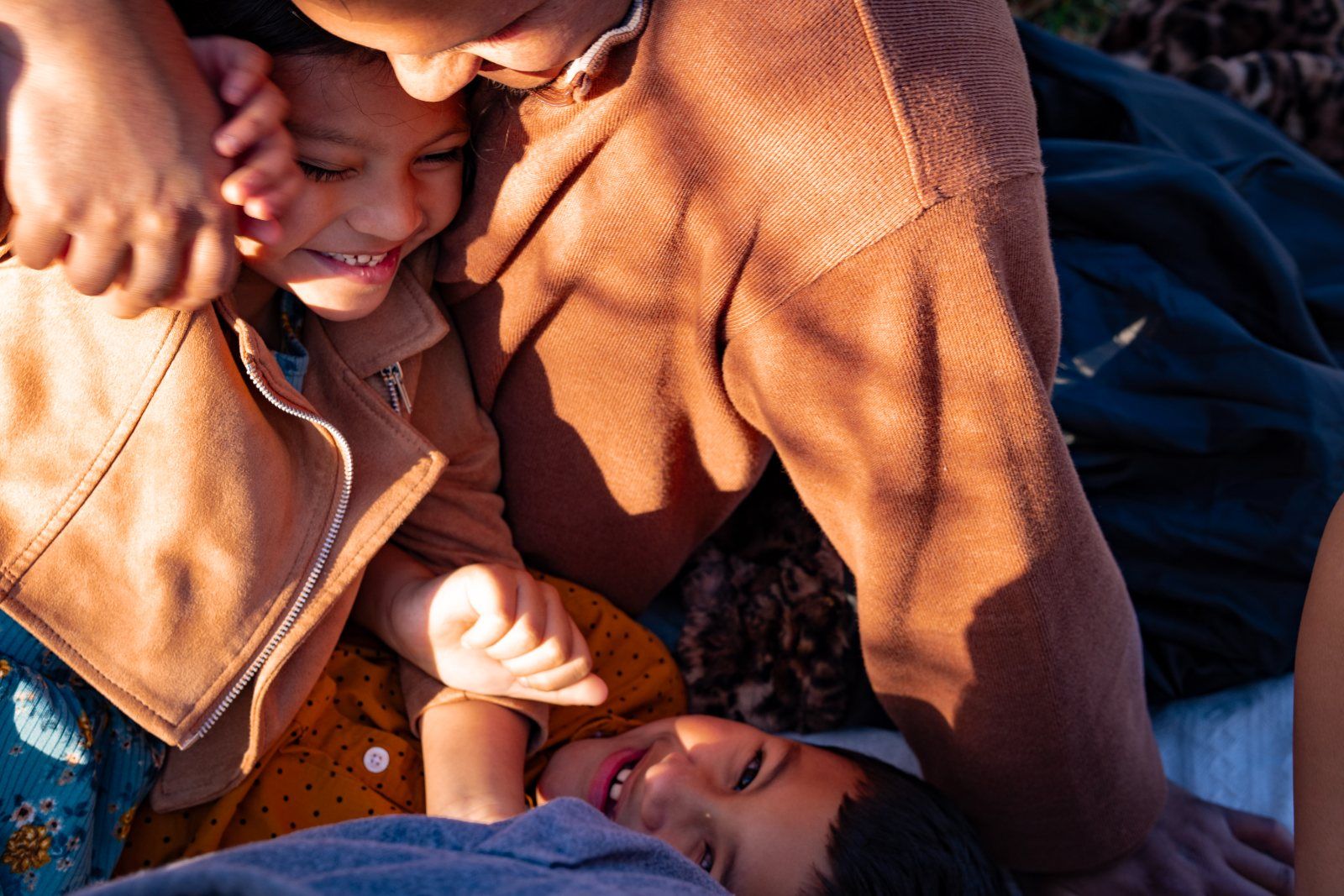 A family laughing in a close tangle on a picnic blanket