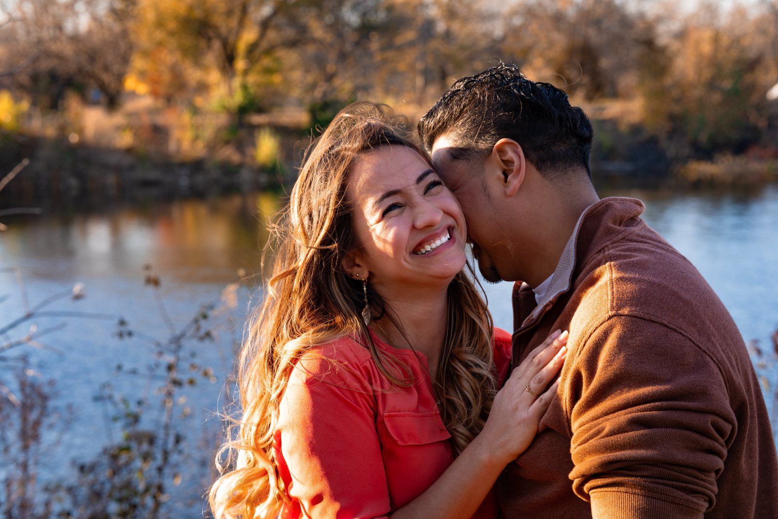 A couple smiling cheek to cheek beside the water at sunset