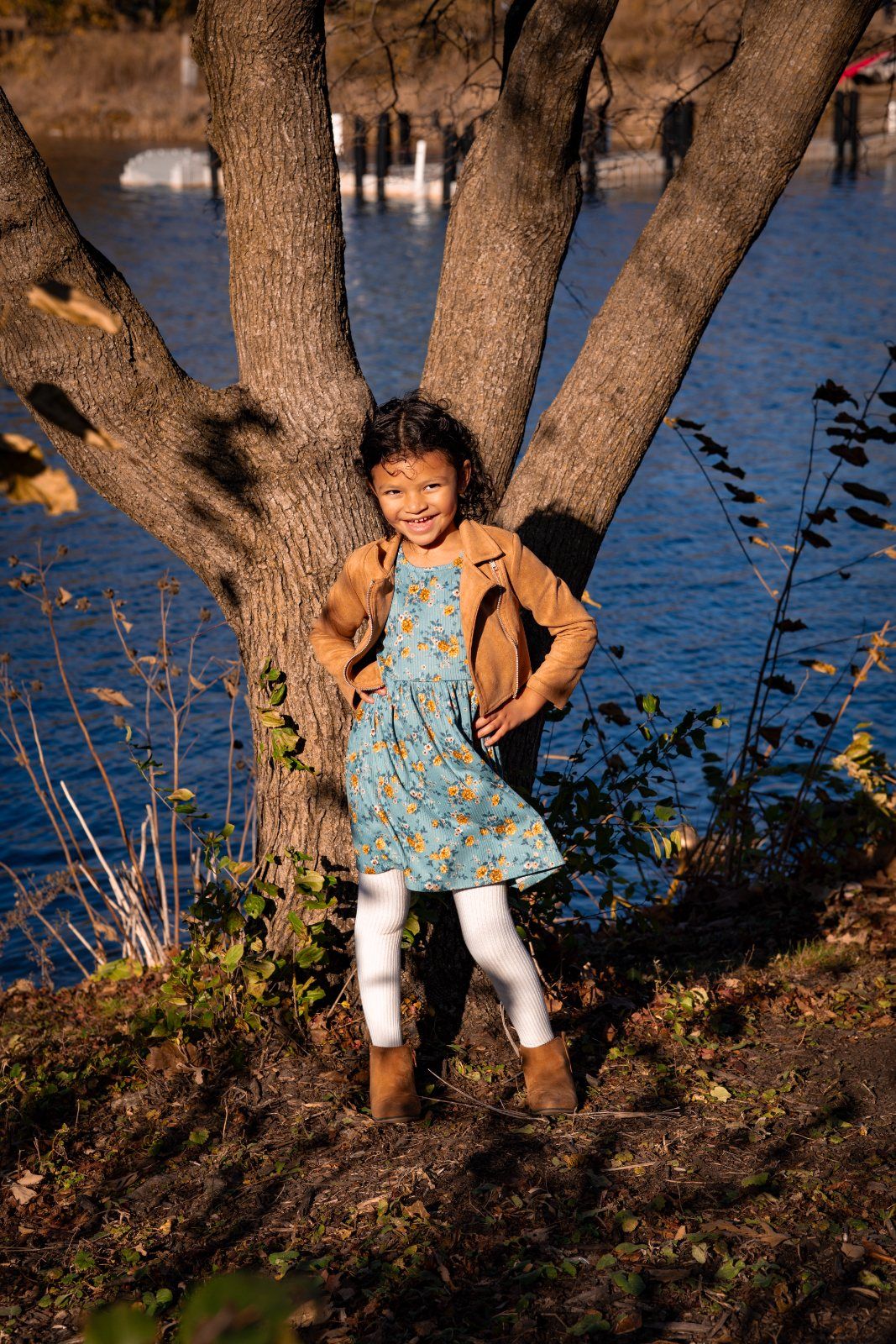 A little girl standing in front of a tree by the lake