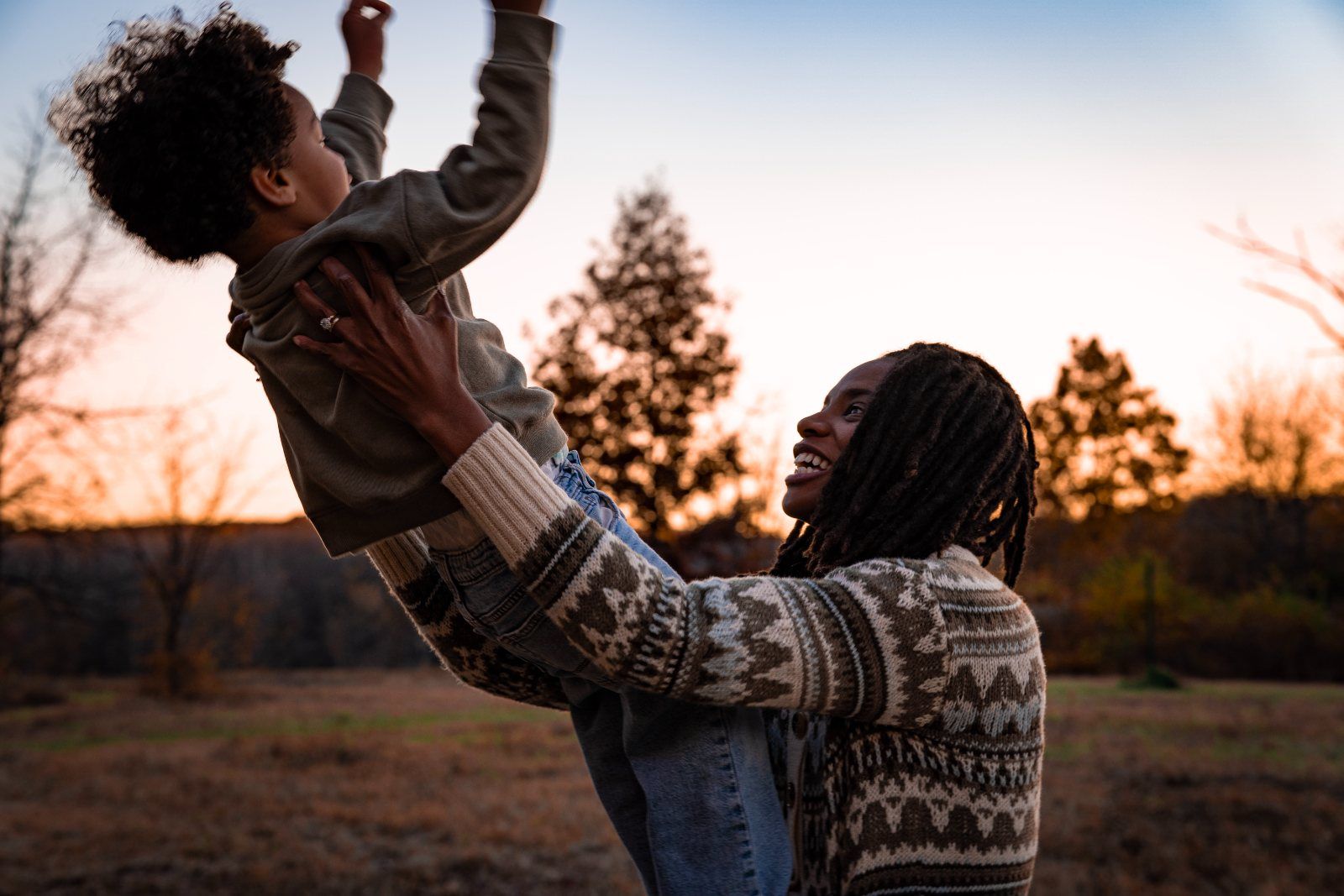 A mother lifting her son into the air against the sunset
